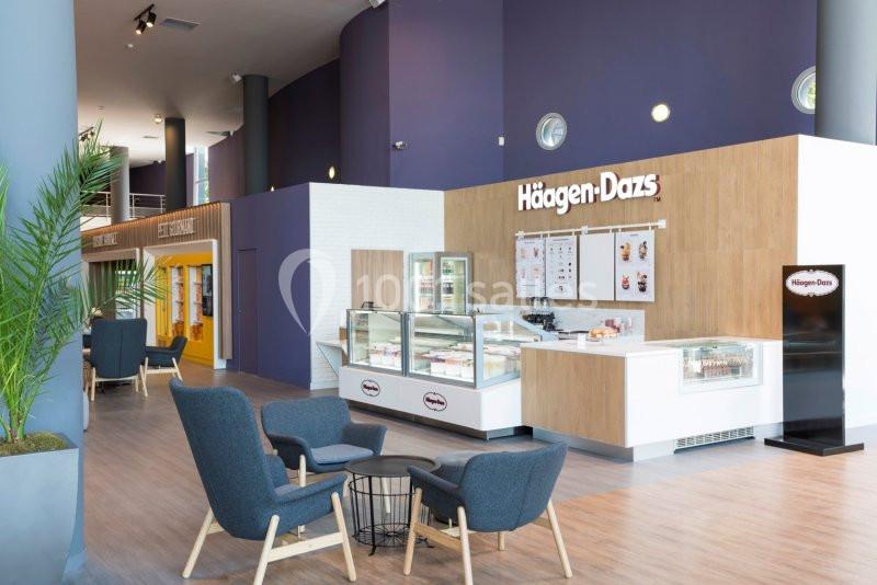 Salon moderne avec comptoir de glaces, vitrines réfrigérées, fauteuils confortables et décor aux tons violets et bois.