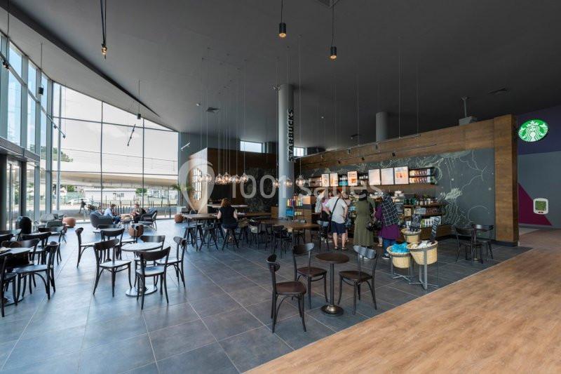 Intérieur d'un café spacieux avec des tables, des chaises, un comptoir de commande et des clients en file.