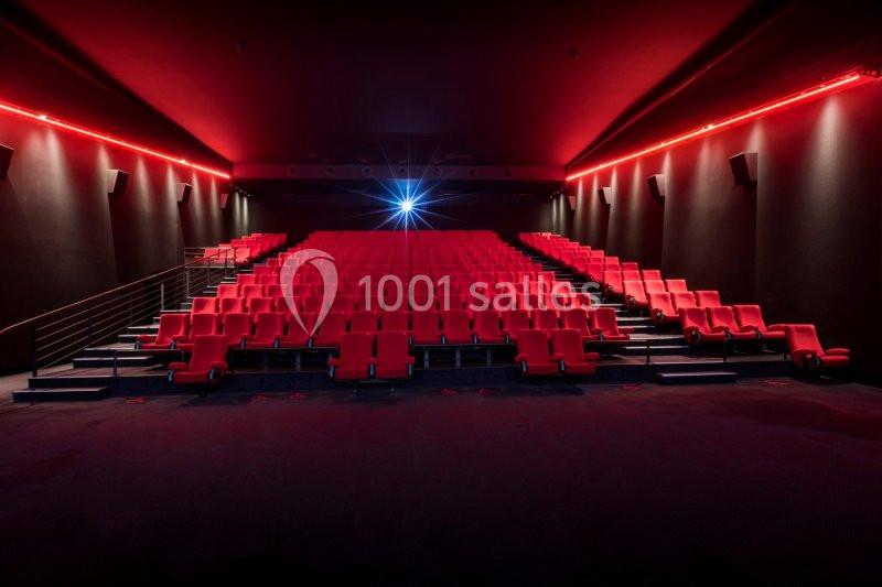 Salle de cinéma vide avec rangées de fauteuils rouges et un projecteur allumé au fond.