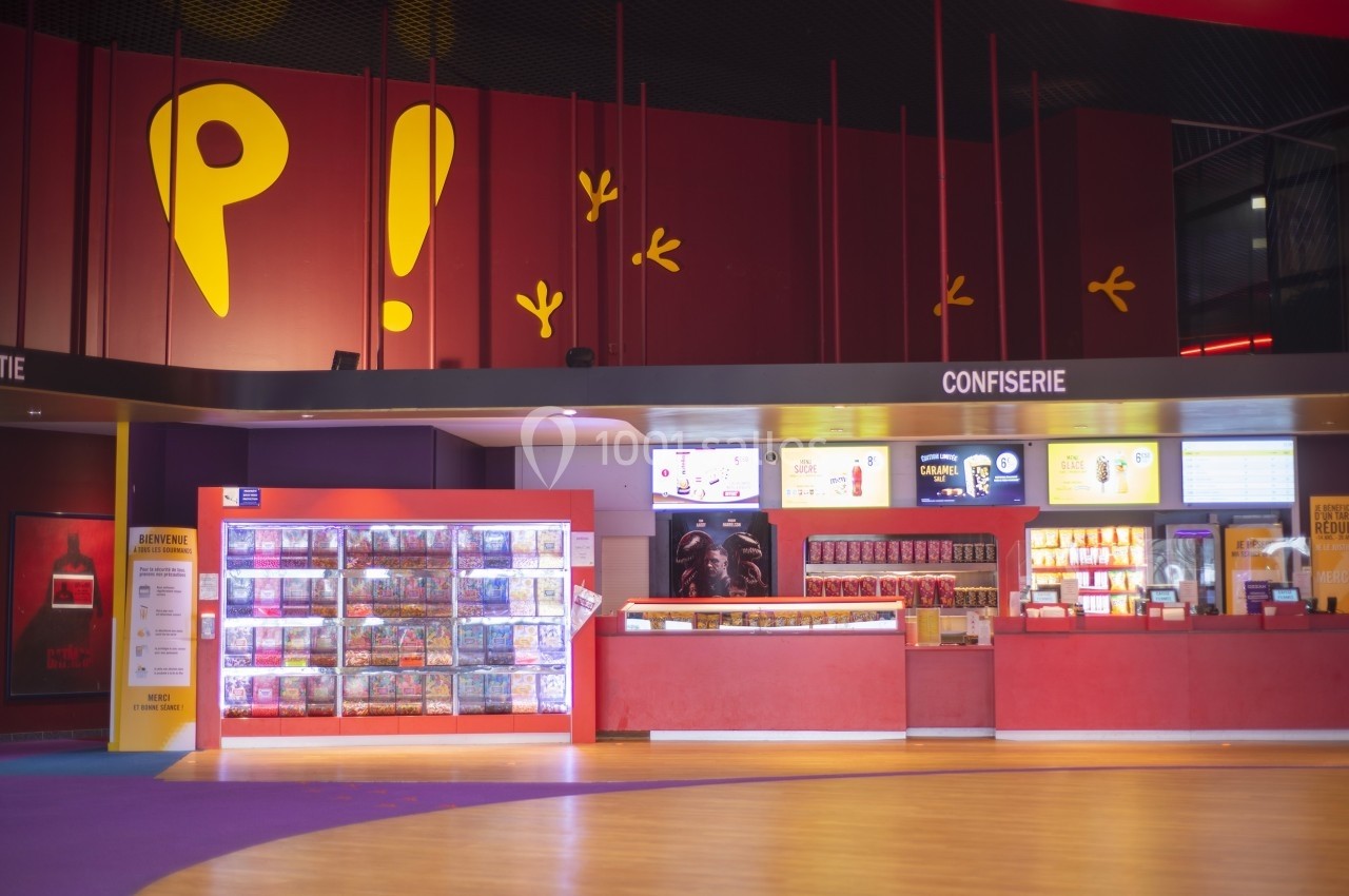 Comptoir de confiserie dans un cinéma avec présentoirs de bonbons, affiches et menus lumineux en arrière-plan.