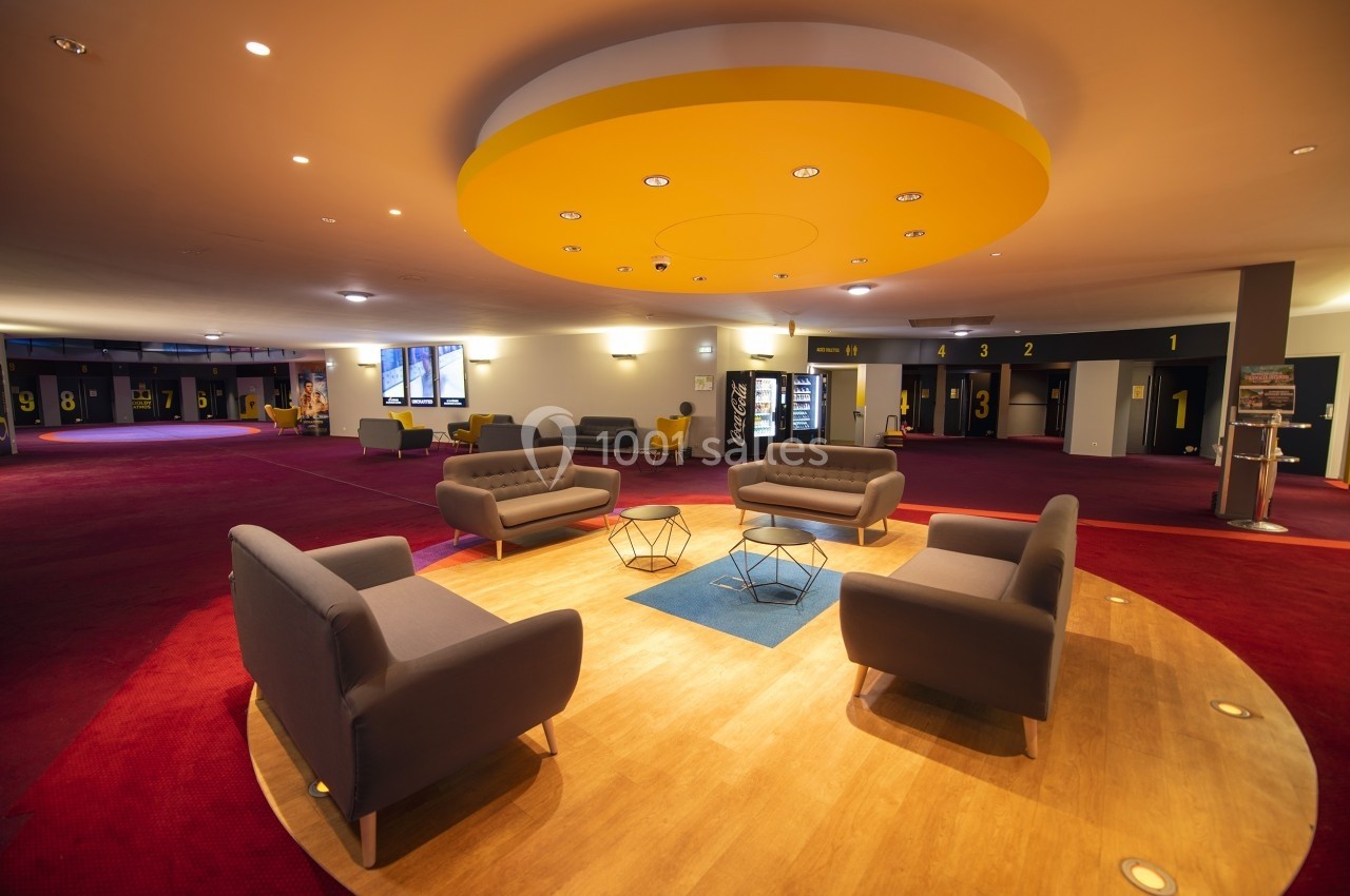 Espace d'attente moderne avec fauteuils gris, tables basses et éclairage circulaire jaune au plafond.