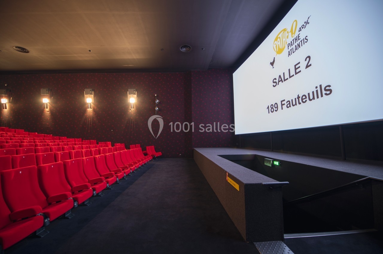 Salle de cinéma vide avec des rangées de fauteuils rouges et un écran affichant ’Salle 2, 189 fauteuils’.