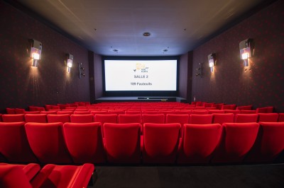 Salle de cinéma vide avec rangées de fauteuils rouges alignés face à un écran non visible.