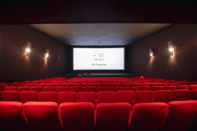 Salle de cinéma vide avec rangées de fauteuils rouges alignés face à un écran non visible.