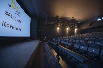 Salle de cinéma vide avec rangées de fauteuils rouges alignés face à un écran non visible.