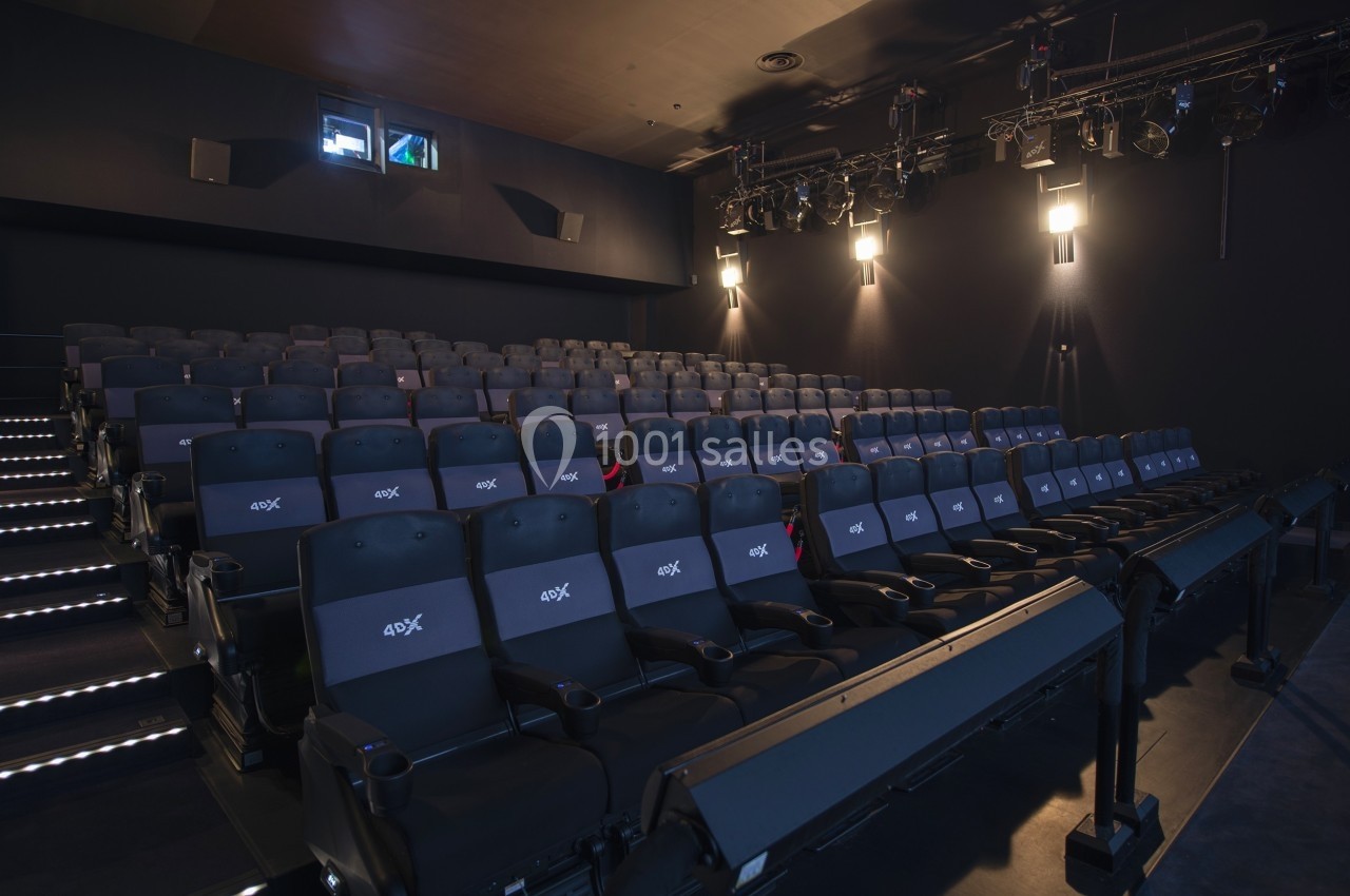 Salle de cinéma vide avec des sièges 4DX, éclairage tamisé et équipements techniques visibles au plafond.