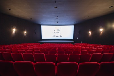 Salle de cinéma vide avec rangées de fauteuils rouges alignés face à un écran non visible.