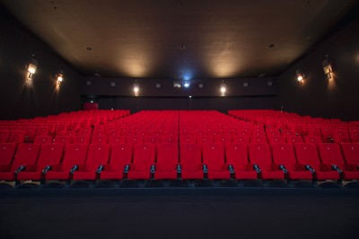 Salle de cinéma vide avec rangées de fauteuils rouges alignés face à un écran non visible.