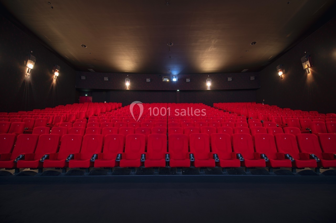 Salle de cinéma vide avec rangées de fauteuils rouges alignés face à un écran non visible.