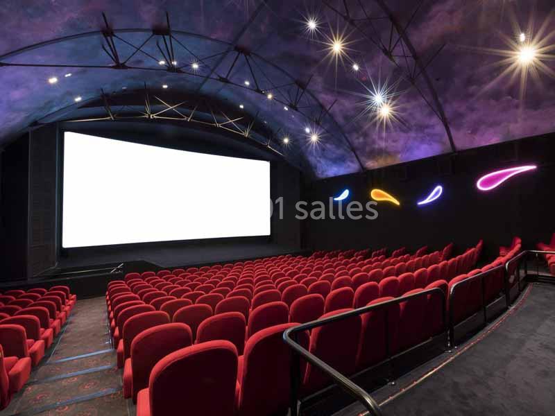 Salle de cinéma vide avec des rangées de sièges rouges, un écran blanc et un plafond décoré d'étoiles.