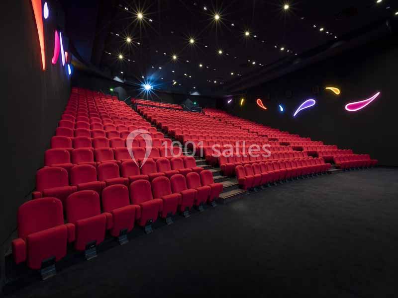 Salle de cinéma vide avec des rangées de sièges rouges et des décorations lumineuses sur les murs sombres.