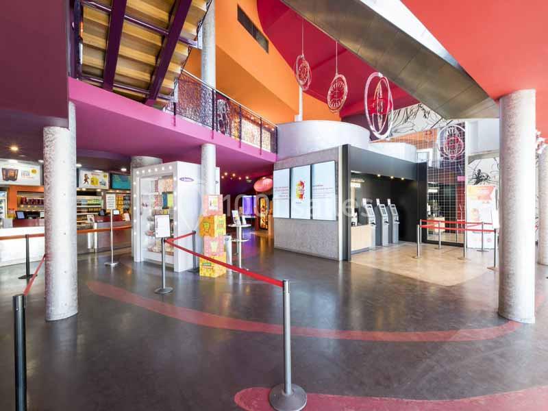 Hall d'entrée d'un cinéma avec bornes automatiques, comptoir de vente et décor coloré.