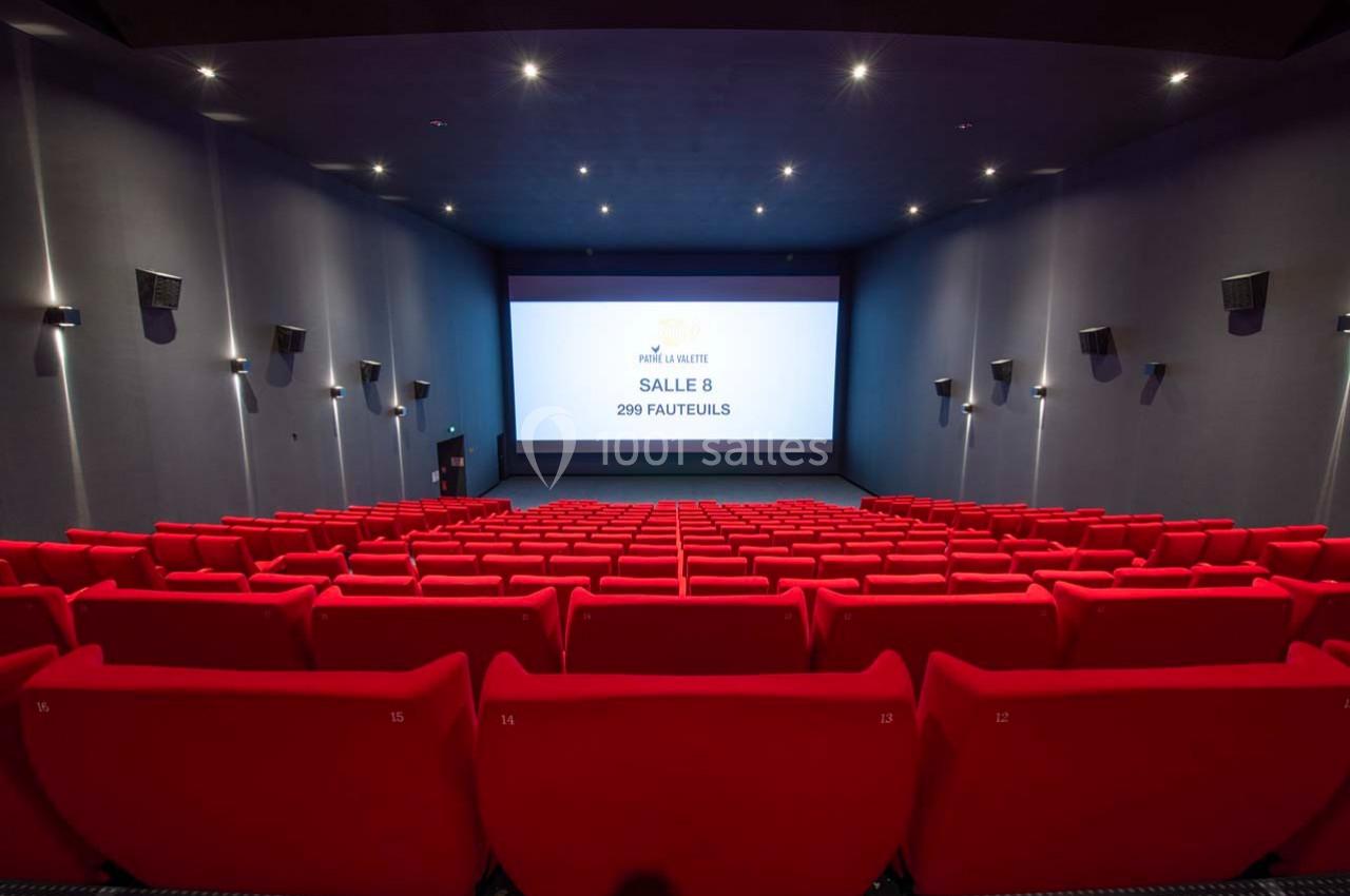 Salle de cinéma vide avec des rangées de fauteuils rouges et un écran affichant ’Salle 8, 299 fauteuils’.