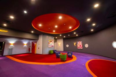 Salle colorée avec moquette violette et orange, plafond circulaire rouge, chaises modernes et affiches murales.
