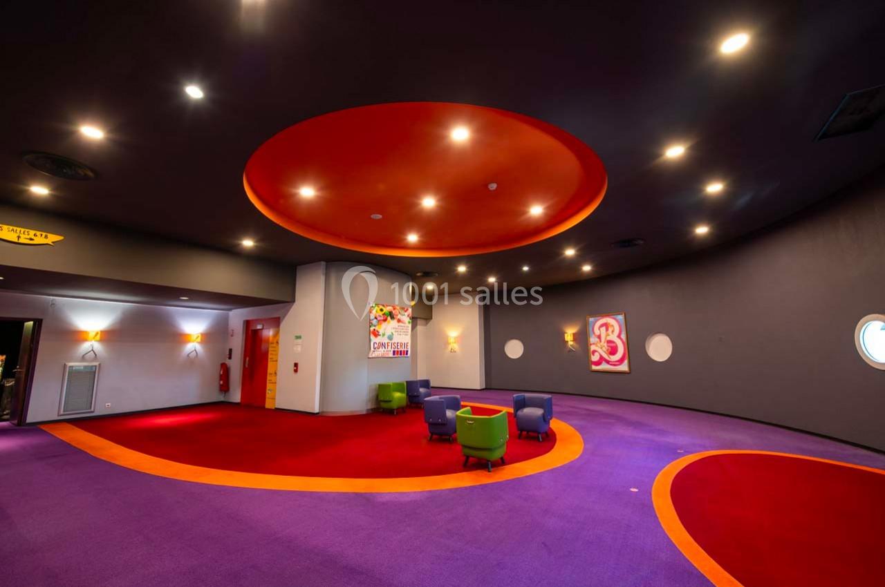 Salle colorée avec moquette violette et orange, plafond circulaire rouge, chaises modernes et affiches murales.