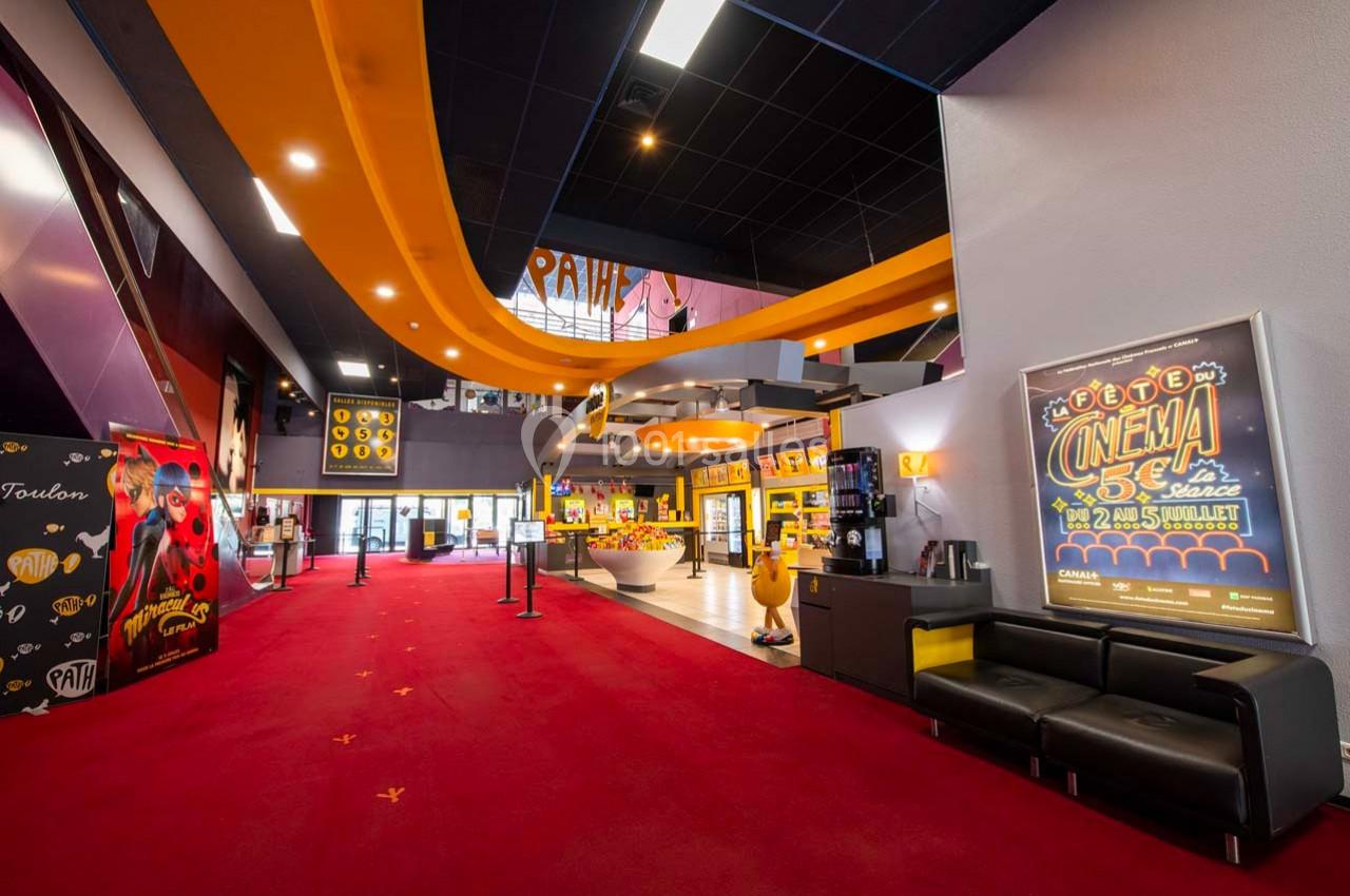 Hall d'entrée d'un cinéma avec tapis rouge, affiches promotionnelles et comptoir de confiseries lumineux.