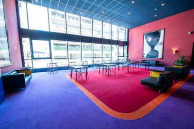 Salle colorée avec moquette violette et orange, plafond circulaire rouge, chaises modernes et affiches murales.