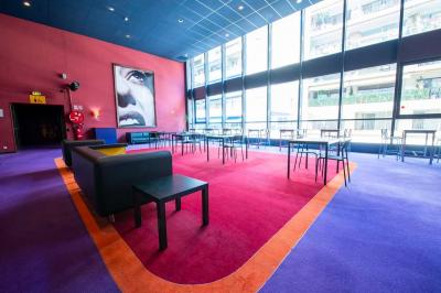Salle colorée avec moquette violette et orange, plafond circulaire rouge, chaises modernes et affiches murales.