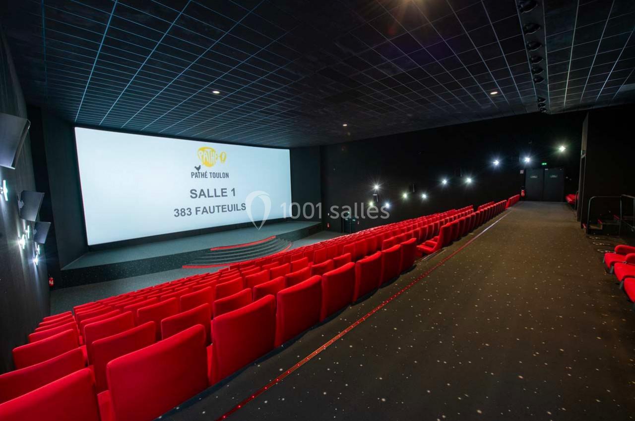 Salle de cinéma moderne avec des rangées de fauteuils rouges, un écran géant et un sol en moquette sombre.