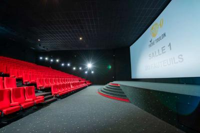 Salle colorée avec moquette violette et orange, plafond circulaire rouge, chaises modernes et affiches murales.