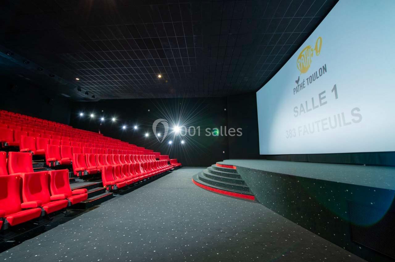 Salle de cinéma moderne avec sièges rouges, écran géant affichant ’Salle 1’ et éclairage tamisé.
