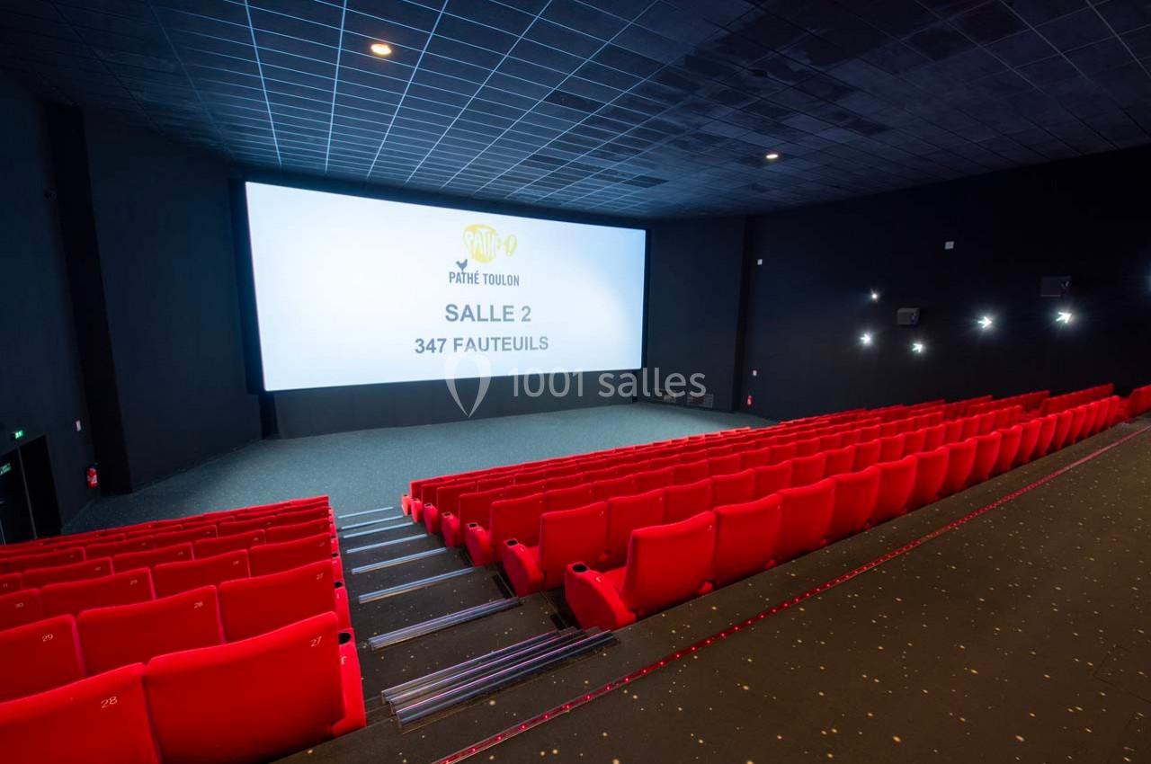 Salle de cinéma vide avec rangées de fauteuils rouges, grand écran affichant ’Salle 2, 347 fauteuils’.