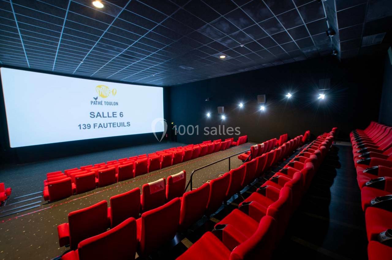 Salle de cinéma avec des rangées de fauteuils rouges, un grand écran blanc affichant des informations sur la salle.