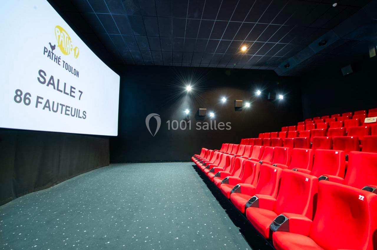 Salle de cinéma vide avec des sièges rouges, écran affichant ’Pathé Toulon Salle 7, 86 fauteuils’ et éclairage tamisé.