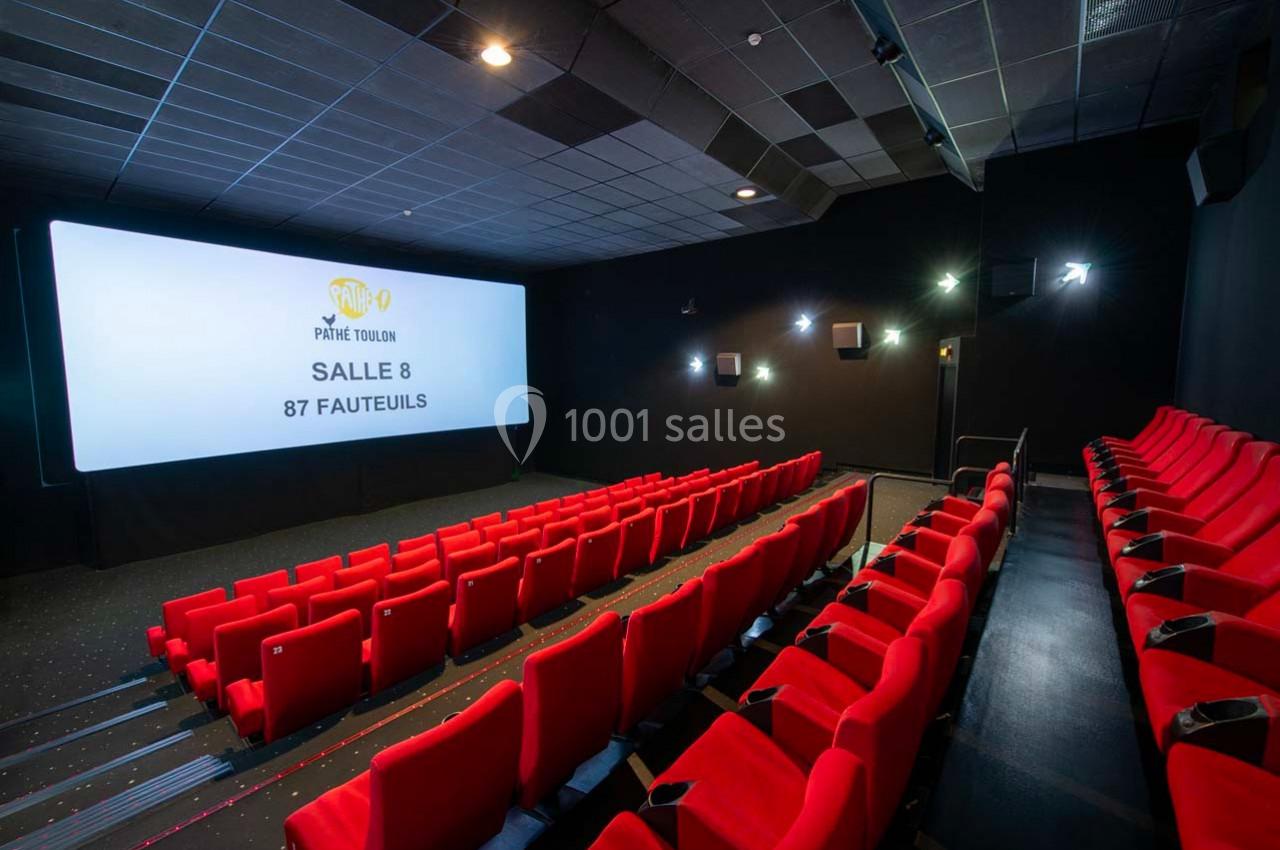 Salle de cinéma avec écran large, rangées de fauteuils rouges et éclairage tamisé.