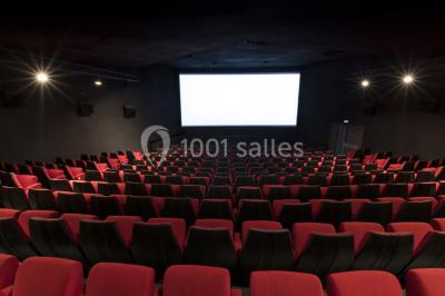 Salle de cinéma vide avec rangées de sièges rouges alignés et éclairage tamisé.