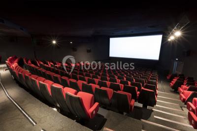 Salle de cinéma vide avec rangées de sièges rouges alignés et éclairage tamisé.