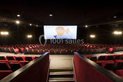 Salle de cinéma vide avec rangées de sièges rouges alignés et éclairage tamisé.
