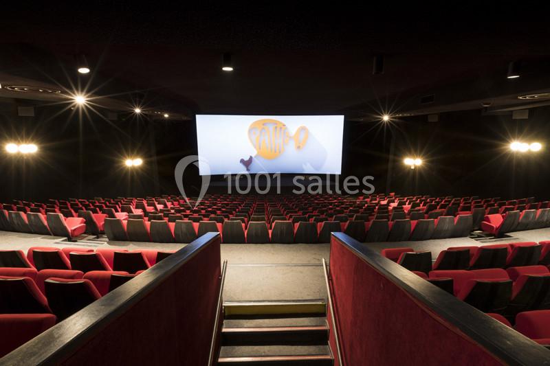 Salle de cinéma vide avec des rangées de fauteuils rouges et un grand écran allumé au fond.