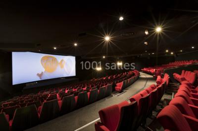 Salle de cinéma vide avec rangées de sièges rouges alignés et éclairage tamisé.