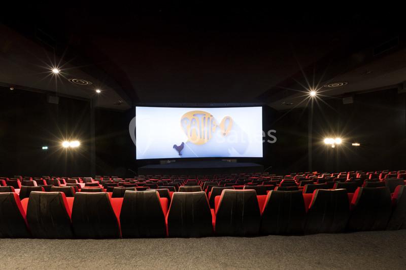 Salle de cinéma vide avec des rangées de fauteuils rouges et un grand écran affichant un logo lumineux.