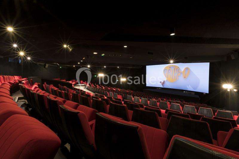 Salle de cinéma vide avec des sièges rouges et un grand écran affichant un logo lumineux.