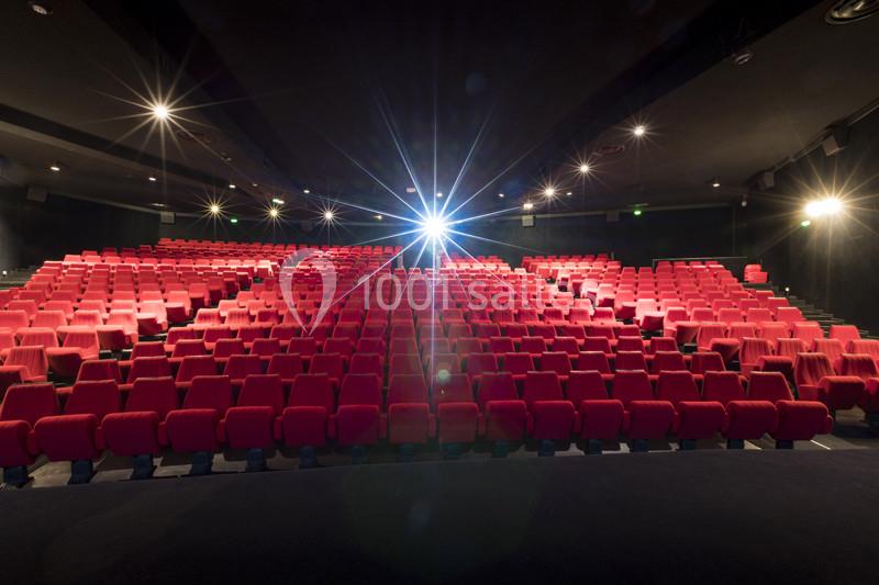 Salle de cinéma vide avec des rangées de sièges rouges et un projecteur allumé au fond.