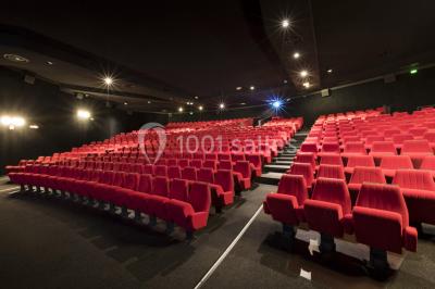 Salle de cinéma vide avec rangées de sièges rouges alignés et éclairage tamisé.