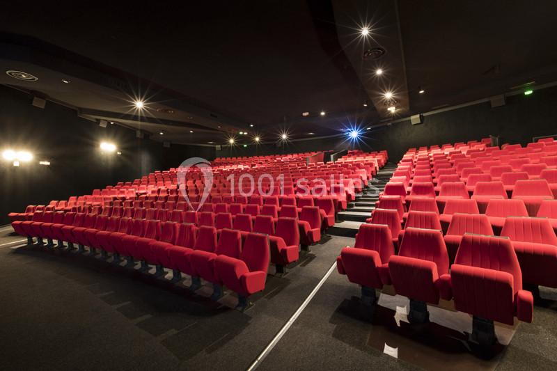 Salle de cinéma vide avec des rangées de sièges rouges et un éclairage tamisé.