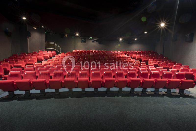 Salle de cinéma vide avec rangées de sièges rouges alignés face à un écran hors champ.