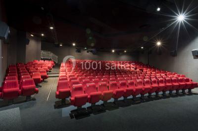 Salle de cinéma vide avec rangées de sièges rouges alignés et éclairage tamisé.