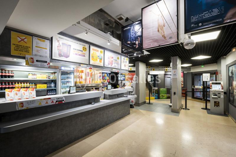 Comptoir de vente dans un cinéma avec affiches, écrans, boissons et snacks exposés.