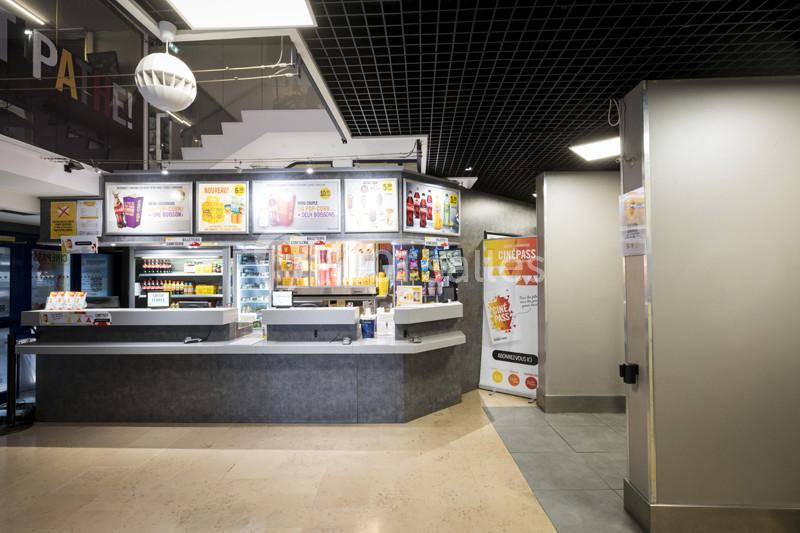 Comptoir de confiseries et boissons dans un hall de cinéma, avec affiches et éclairage lumineux.