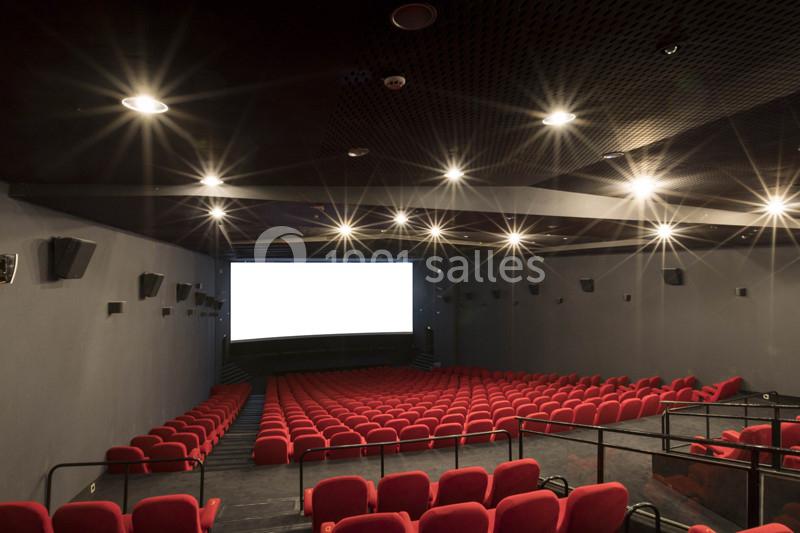 Salle de cinéma vide avec des sièges rouges, un écran blanc et un éclairage tamisé au plafond.