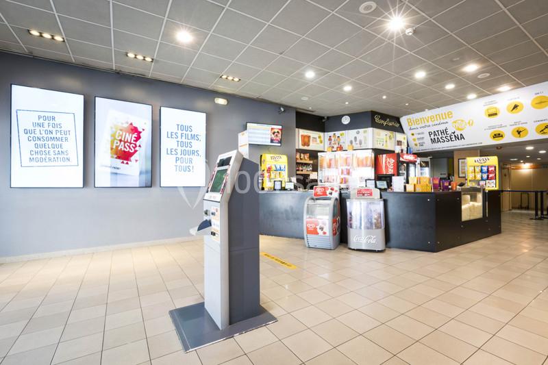 Hall d'entrée d'un cinéma avec bornes interactives, affiches promotionnelles et comptoir de confiseries éclairé.
