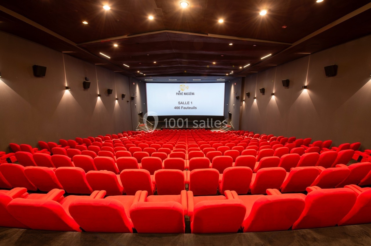 Salle de cinéma vide avec des rangées de fauteuils rouges et un écran blanc au fond.