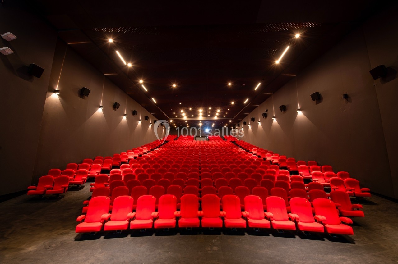 Salle de cinéma vide avec des rangées de fauteuils rouges et un éclairage tamisé.