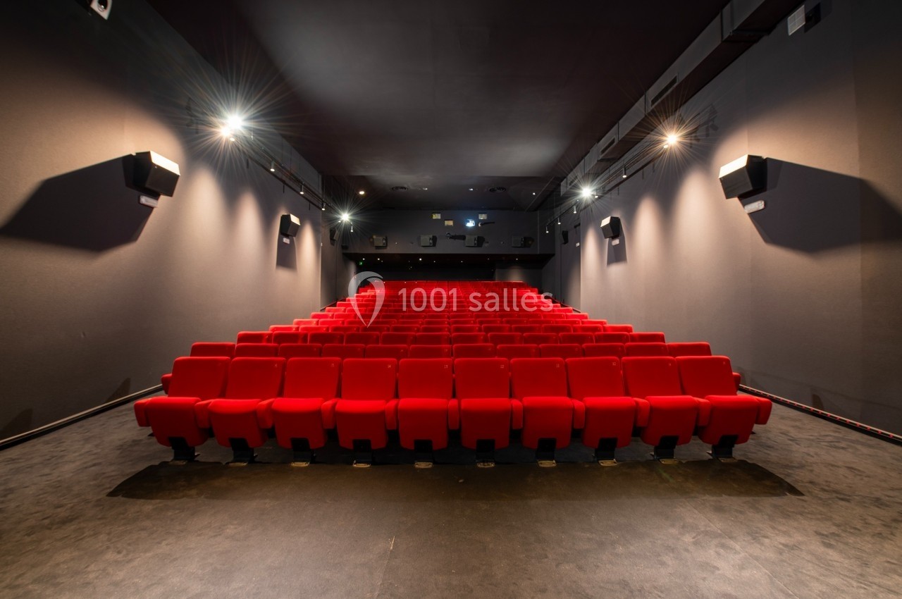 Salle de cinéma vide avec rangées de fauteuils rouges alignés et éclairage tamisé.
