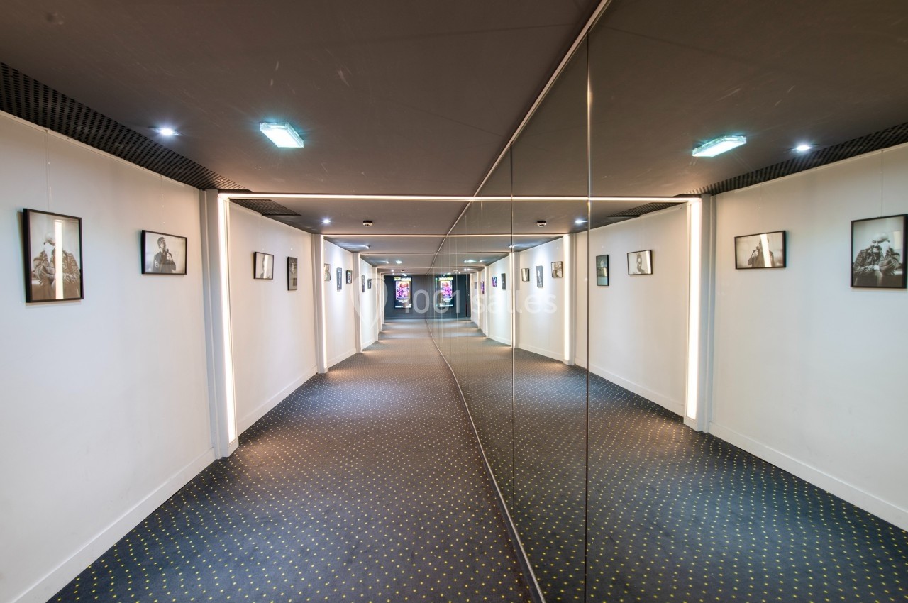 Couloir moderne avec un mur de miroirs à droite, des cadres accrochés à gauche et un sol à motifs géométriques.