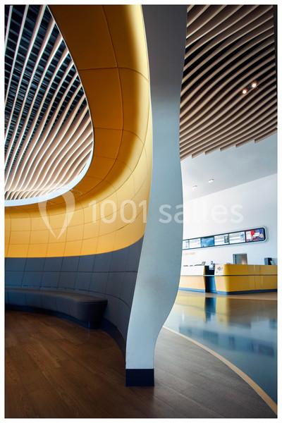 Mur courbé jaune et gris avec des lamelles en bois au plafond, vue sur un comptoir moderne en arrière-plan.